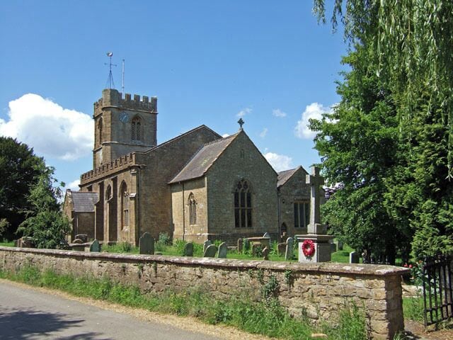 A stone church with a bell tower and a stone wall in front.