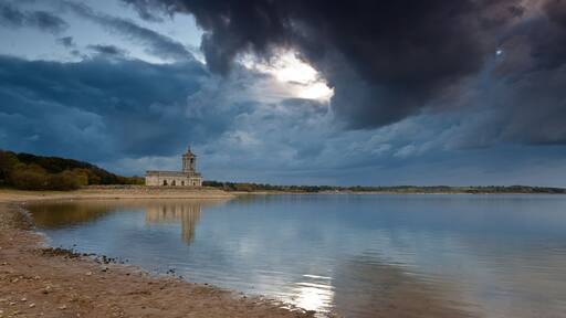 A calm lake with a historic building and a stormy sky.
