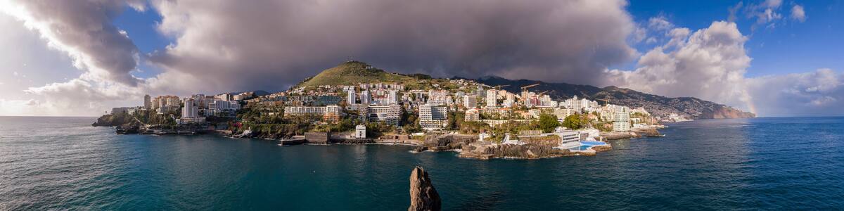 A coastal cityscape with a prominent hill, a rocky outcrop in the water, and a clear sky.