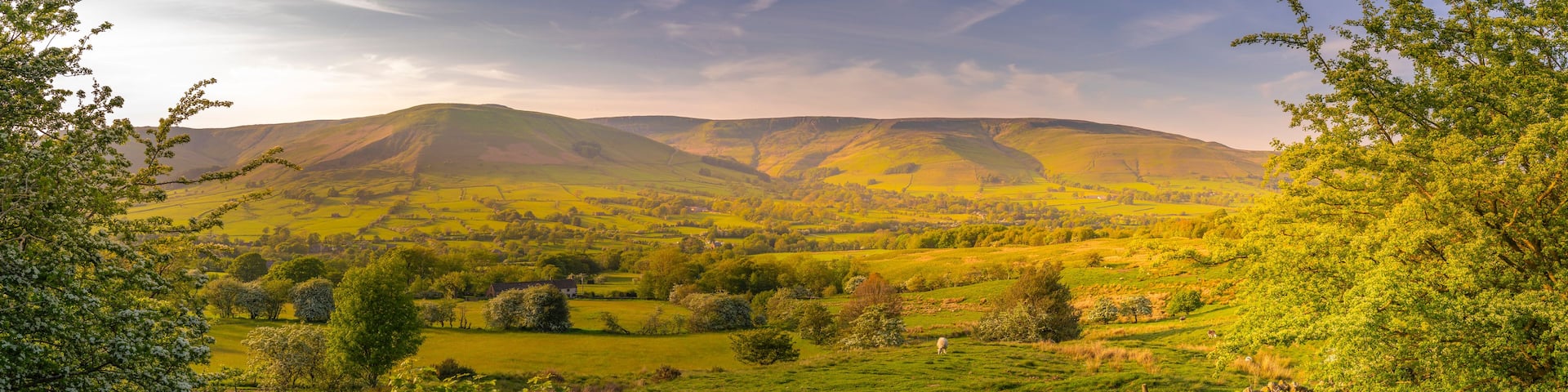 A lush valley with rolling hills, a stone wall, and a distant mountain range.