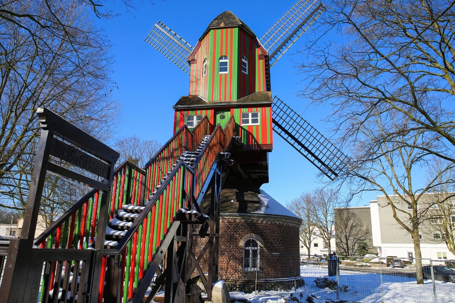 Viersen (Dulken), Germany - February 9. 2021: View beyond steps on red green colorfull striped wind mill (Narrenmuhle) against blue sky in winter