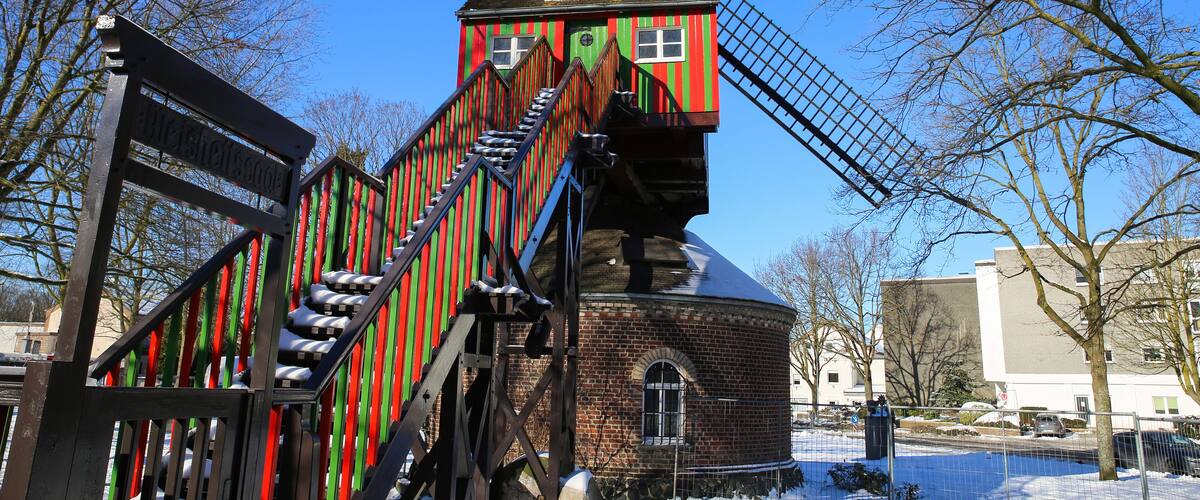 A colorful windmill with a red and green striped facade, a brick base, and a metal staircase leading up to the top.