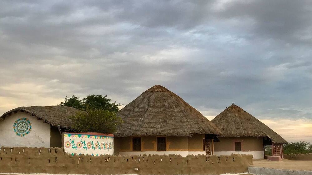 Traditional thatched-roof huts with colorful wall decorations, set against a cloudy sky.