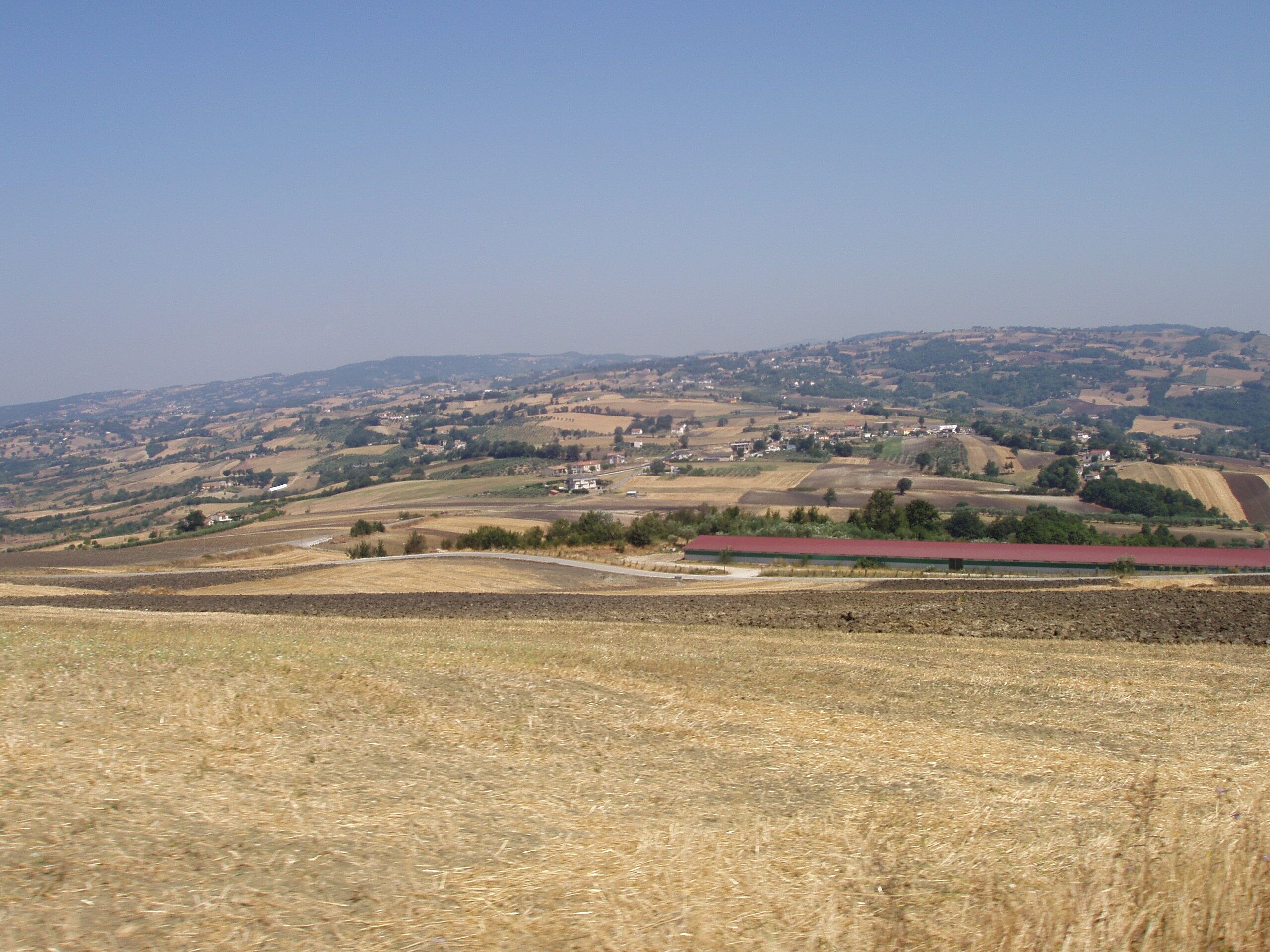 A rural landscape with rolling hills, fields, and scattered buildings.