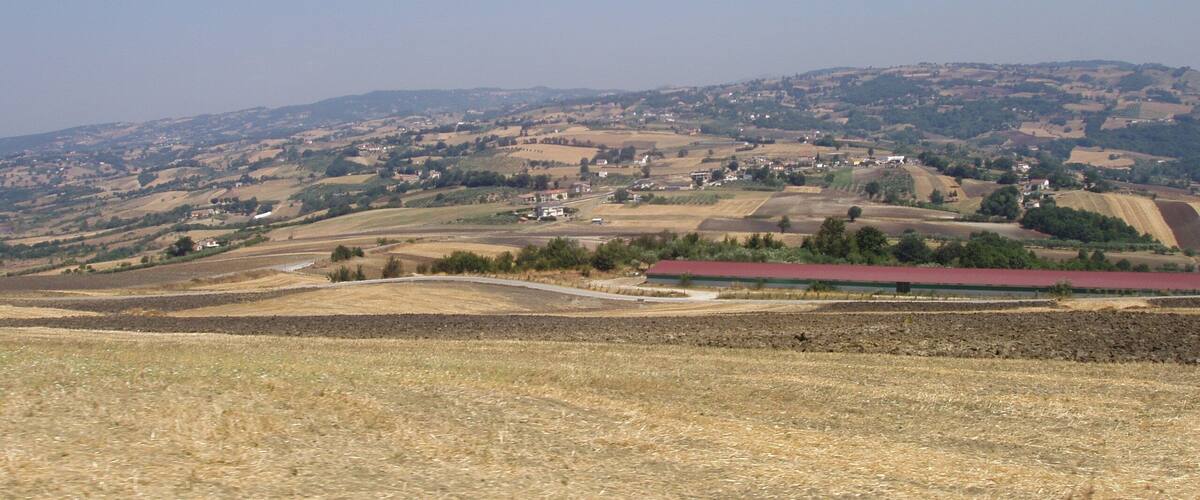 A rural landscape with rolling hills, fields, and scattered buildings.