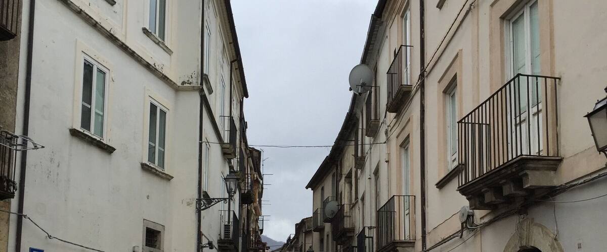 A narrow street flanked by historic buildings with balconies and satellite dishes.