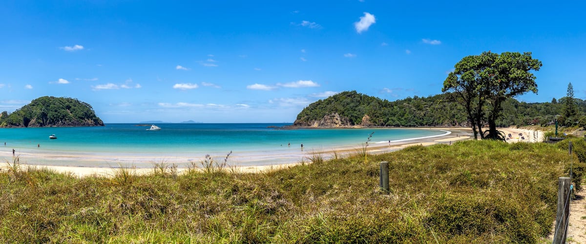 A beach with clear turquoise water, sandy shores, and lush green hills in the background.