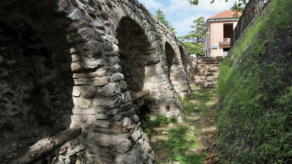 An ancient stone structure with arches and a pathway leading to a modern building.