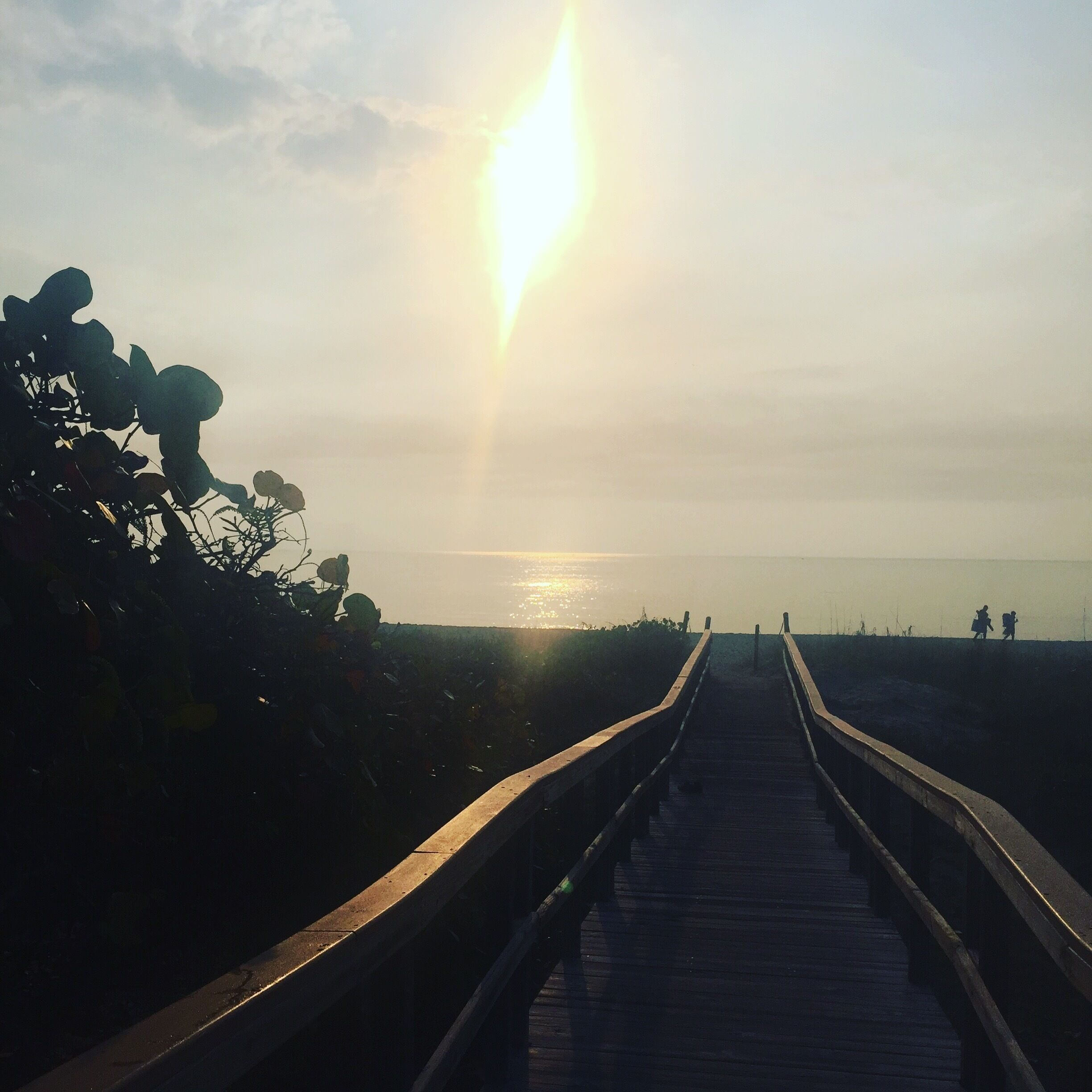 A wooden boardwalk leading to a beach with the sun low on the horizon.