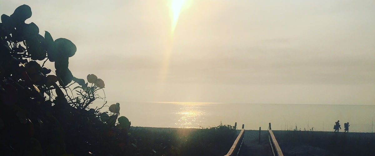 A wooden boardwalk leading to a beach with the sun low on the horizon.