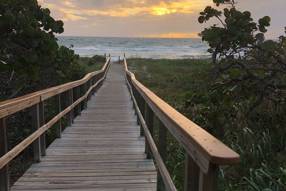 A wooden boardwalk leading to the ocean with a sunset in the background.