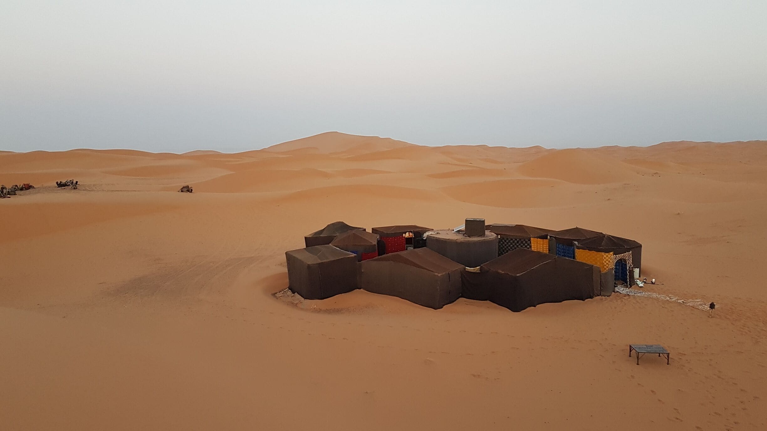 A desert landscape with sand dunes and a cluster of tents.