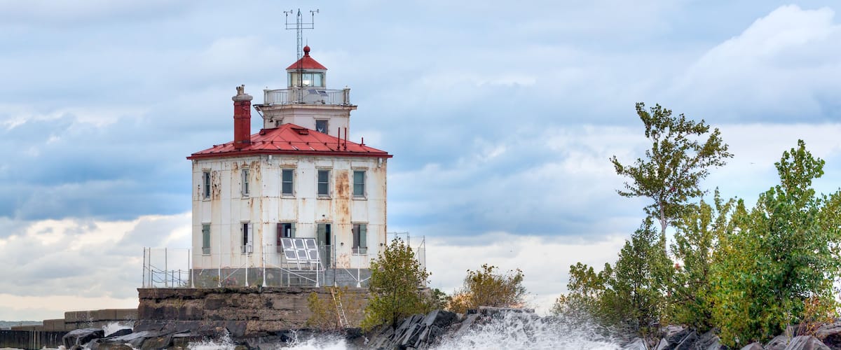 Un phare au bord d’une mer agitée, avec un toit rouge et une girouette.