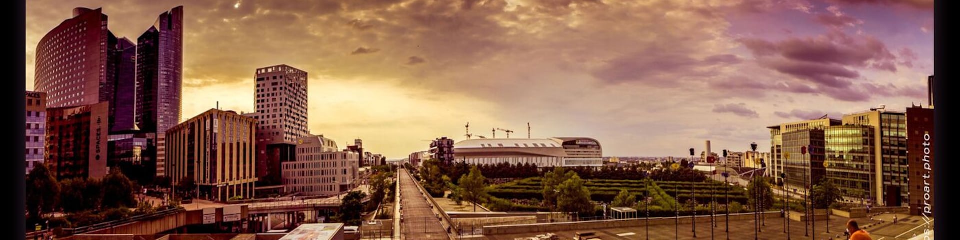 Un paisaje urbano con edificios modernos, un estadio y una persona sentada en el suelo.