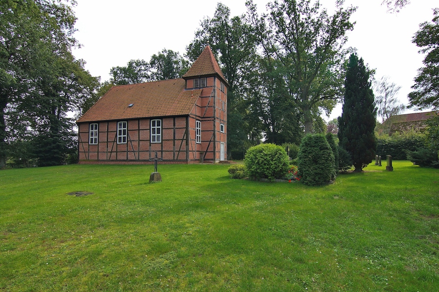 Ett traditionellt hus med korsvirkesfasad och ett brant tak, omgivet av en välskött gräsmatta och fullvuxna träd.