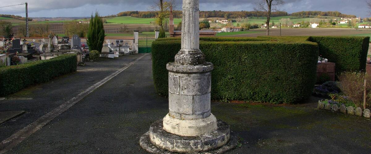 A stone cross in a cemetery with a rural landscape in the background.