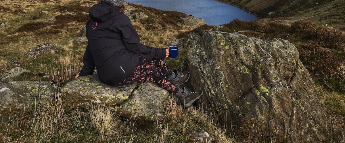 A person sitting on a rock by a lake surrounded by hills.