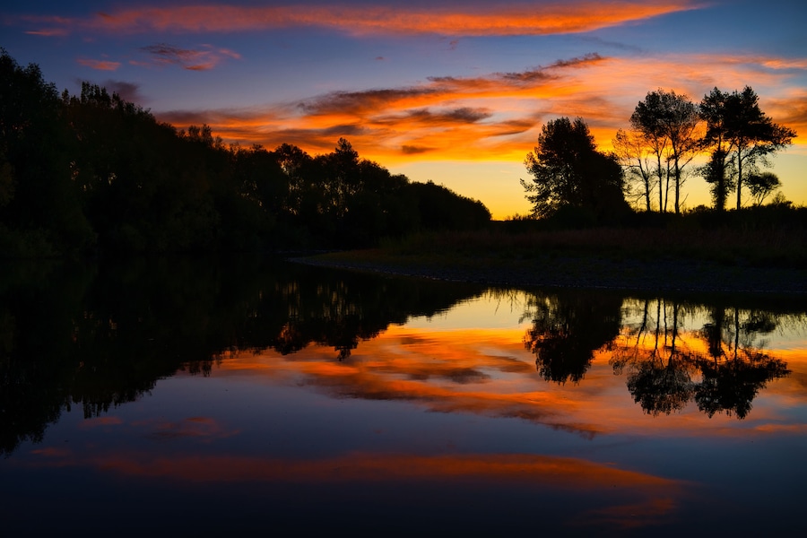 Un atardecer sobre un lago tranquilo, con árboles siluetados contra el cielo.