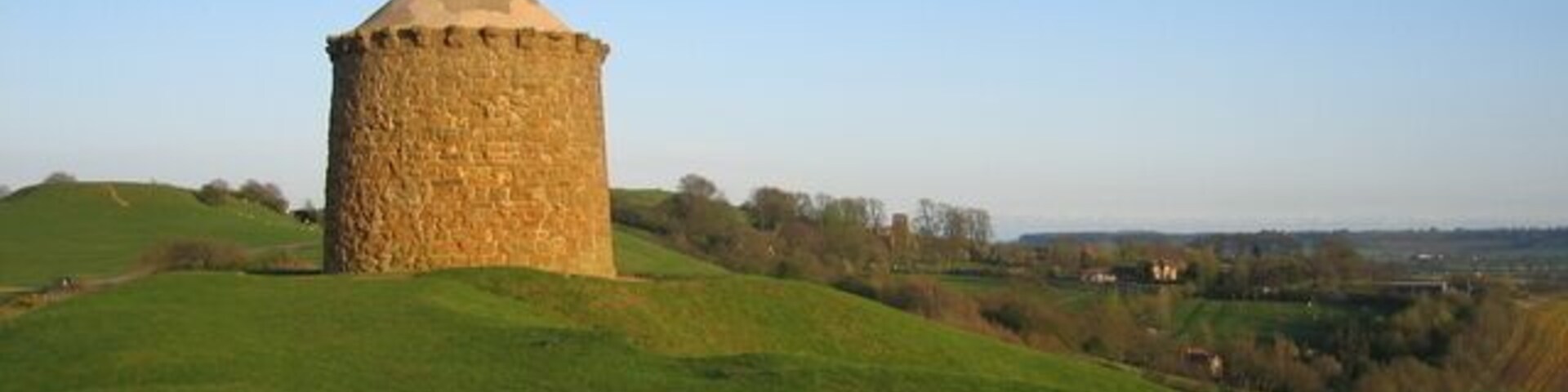 Windmill Hill, Burton Dasset Country Park. The prominent landmark in the Burton Hills now known as 'The Beacon' may have been a windmill. Around 1600 it was known as 'The Lodge'. The earliest reference to it calls it a 'stonmilne' which was working before 1367. The windmill which gives the hill its name was situated alongside and was believed to have been built in 1664 and ceased work in 1912. It was destroyed in a storm in 1946. http://www.roughwood.net/PostcardAlbum/Warwickshire/BurtonDassett/BurtonDassettWindmill.htm Martin Jones has sent in the following interesting reminiscences:- "I remember as a schoolboy the day the windmill blew down in a gale. We all ran up in the evening to look at the wreckage. The granary next to it was open with a window and door missing for years and we (local kids) used to play inside. The day the granary was sealed up by a builder called Mr Thame my brother and I helped mix the cement etc. and we were the last two humans inside before he completely sealed the building. The beacon was open to the elements for many years during and after WWII. Cattle used is as a shelter and we kids used to play inside as well as clambering over the locked sails on the windmill. The powers that be must have decided to restore and seal the building towards the end of the forties - I think! During the celebrations on VE day (1945) a huge bonfire was built on the hill near the beacon which we were told could be seen on the Malvern Hills and beyond."