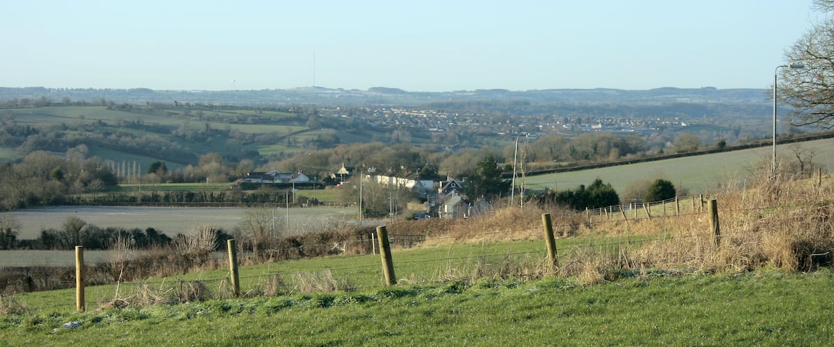 A rural landscape with rolling hills, a small village, and a distant wind turbine.