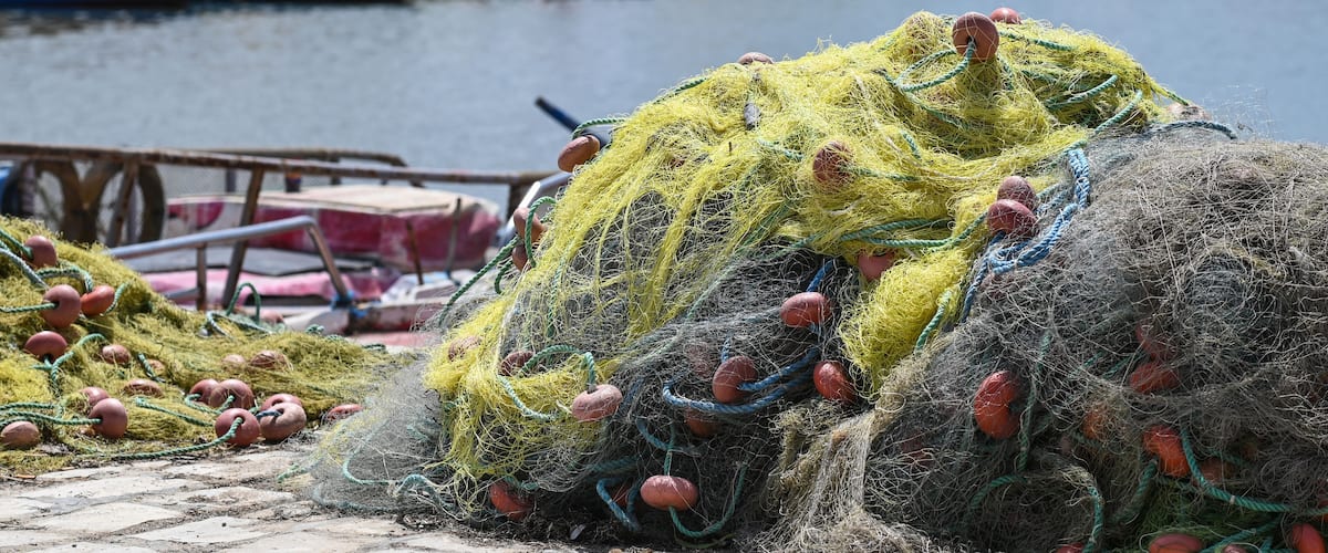 Fishing nets and buoys by a waterfront with boats and colorful umbrellas in the background.
