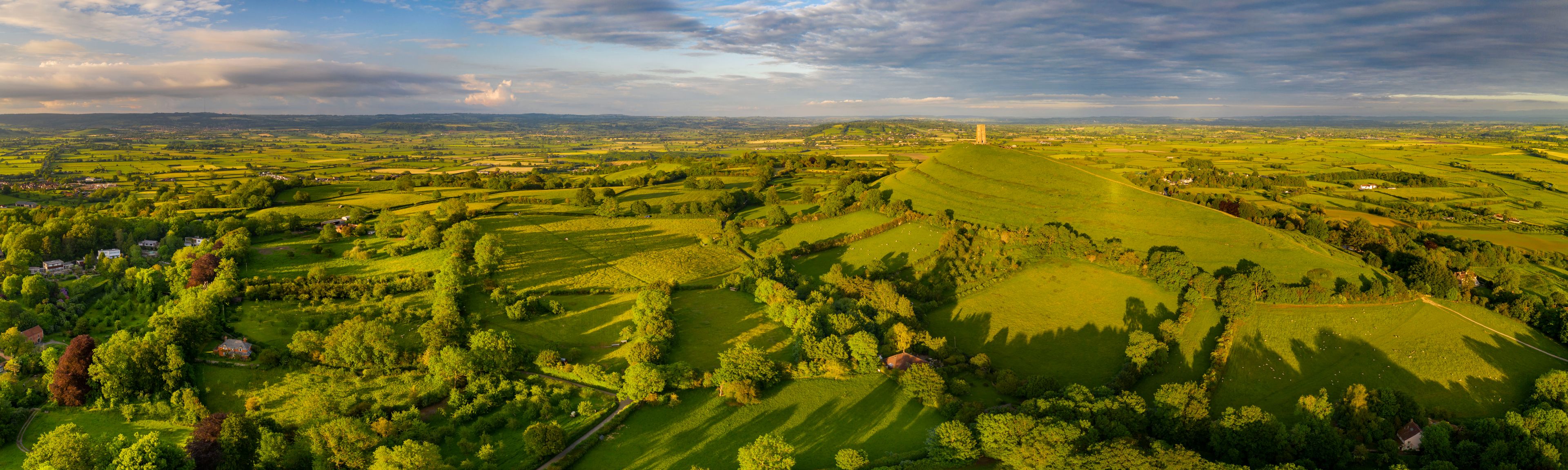 Rolling green hills, a distant tower, and scattered houses.