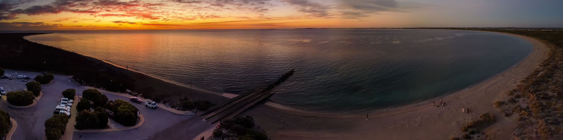 A coastal landscape with a curved road, a beach, and a pier extending into the water.