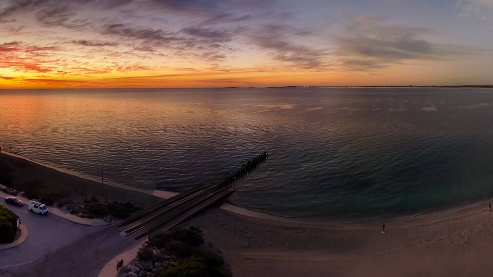 Un paisaje costero con una carretera curva, una playa y un muelle que se adentra en el agua.