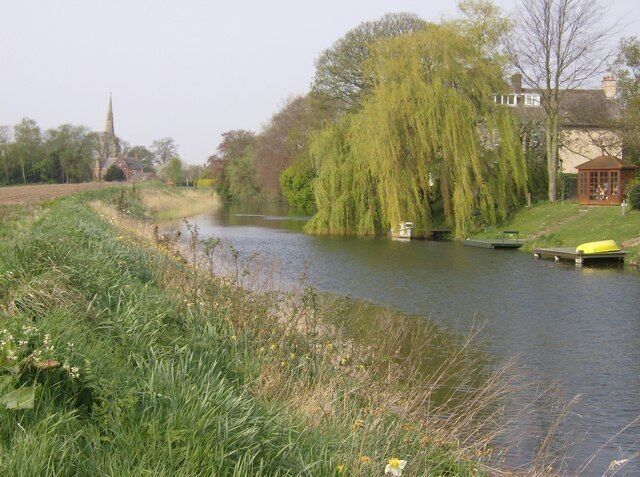 Approaching Surfleet. The River Glen, approaching Surfleet. The gardens of many houses run down to the river, with small boats moored at the bottoms of gardens. A footpath threads its way along the south bank, with arable farmland encroaching.
