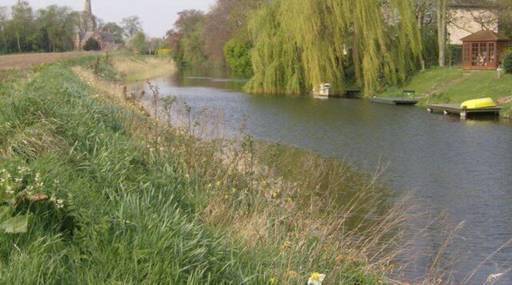 Approaching Surfleet. The River Glen, approaching Surfleet. The gardens of many houses run down to the river, with small boats moored at the bottoms of gardens. A footpath threads its way along the south bank, with arable farmland encroaching.
