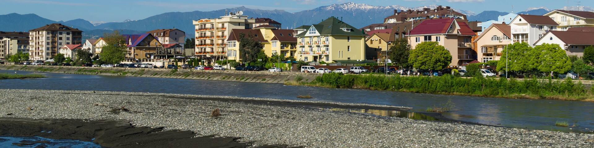 A riverside town with colorful buildings, a river, and mountains in the background.