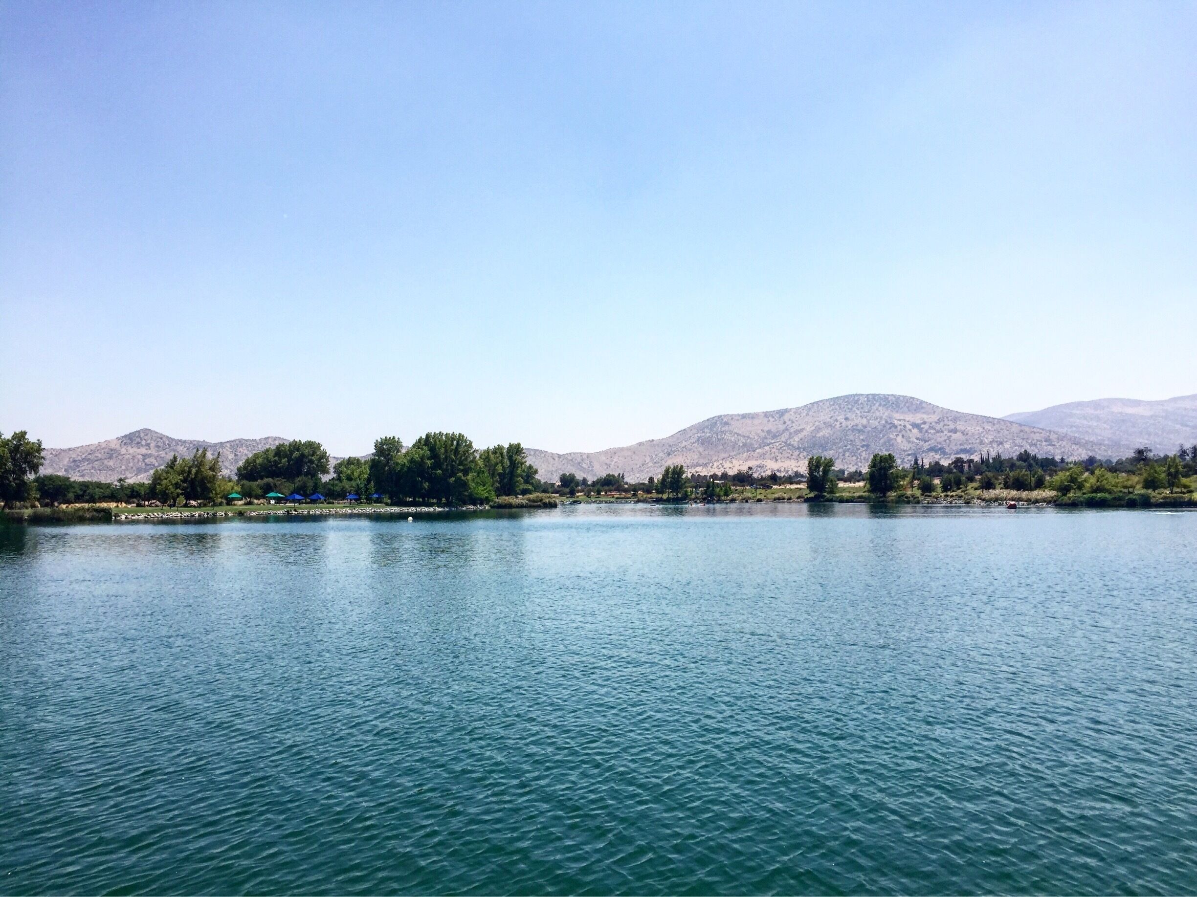 A calm lake with mountains in the background and trees along the shore.