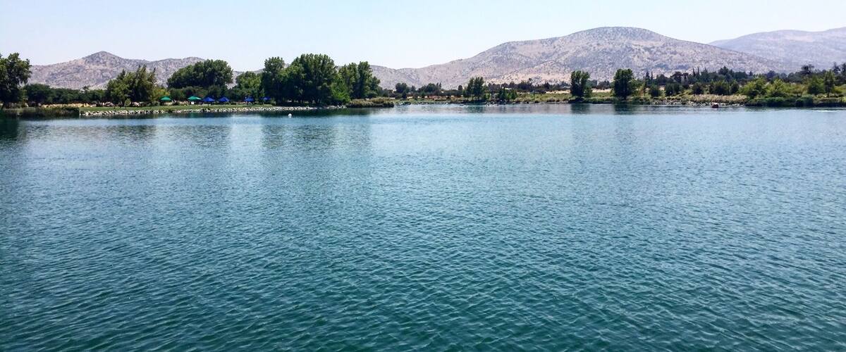 A calm lake with mountains in the background and trees along the shore.