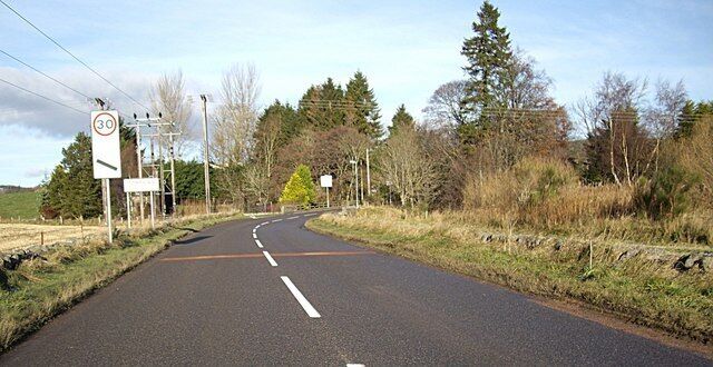 A rural road with a 30 mph speed limit sign, surrounded by trees and open fields.