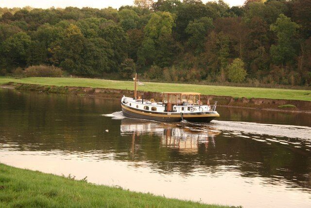 A boat moving on a river with a forested area in the background.