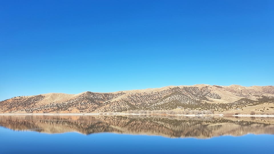 A calm lake reflecting mountains under a clear blue sky.
