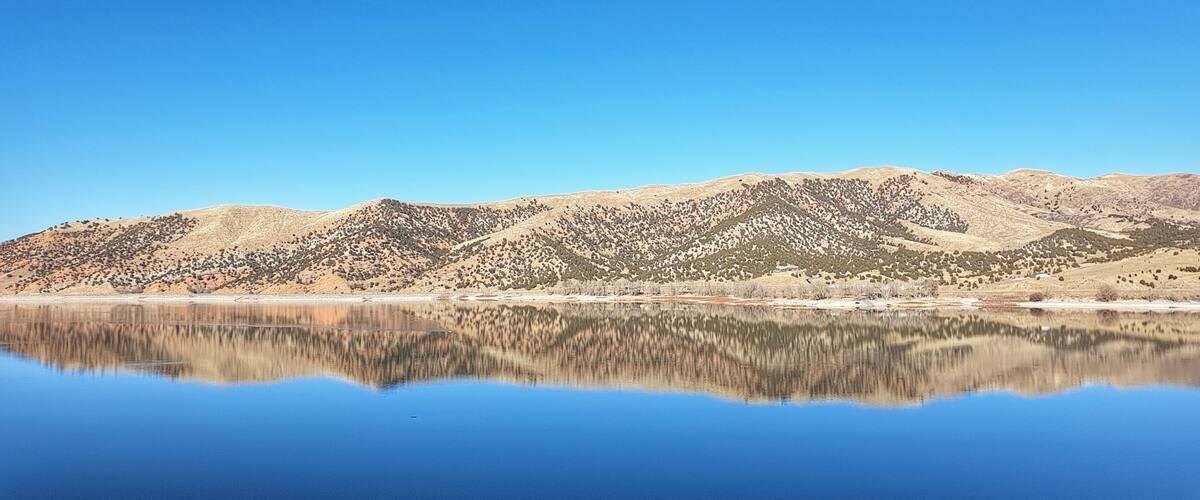 A calm lake reflecting mountains under a clear blue sky.