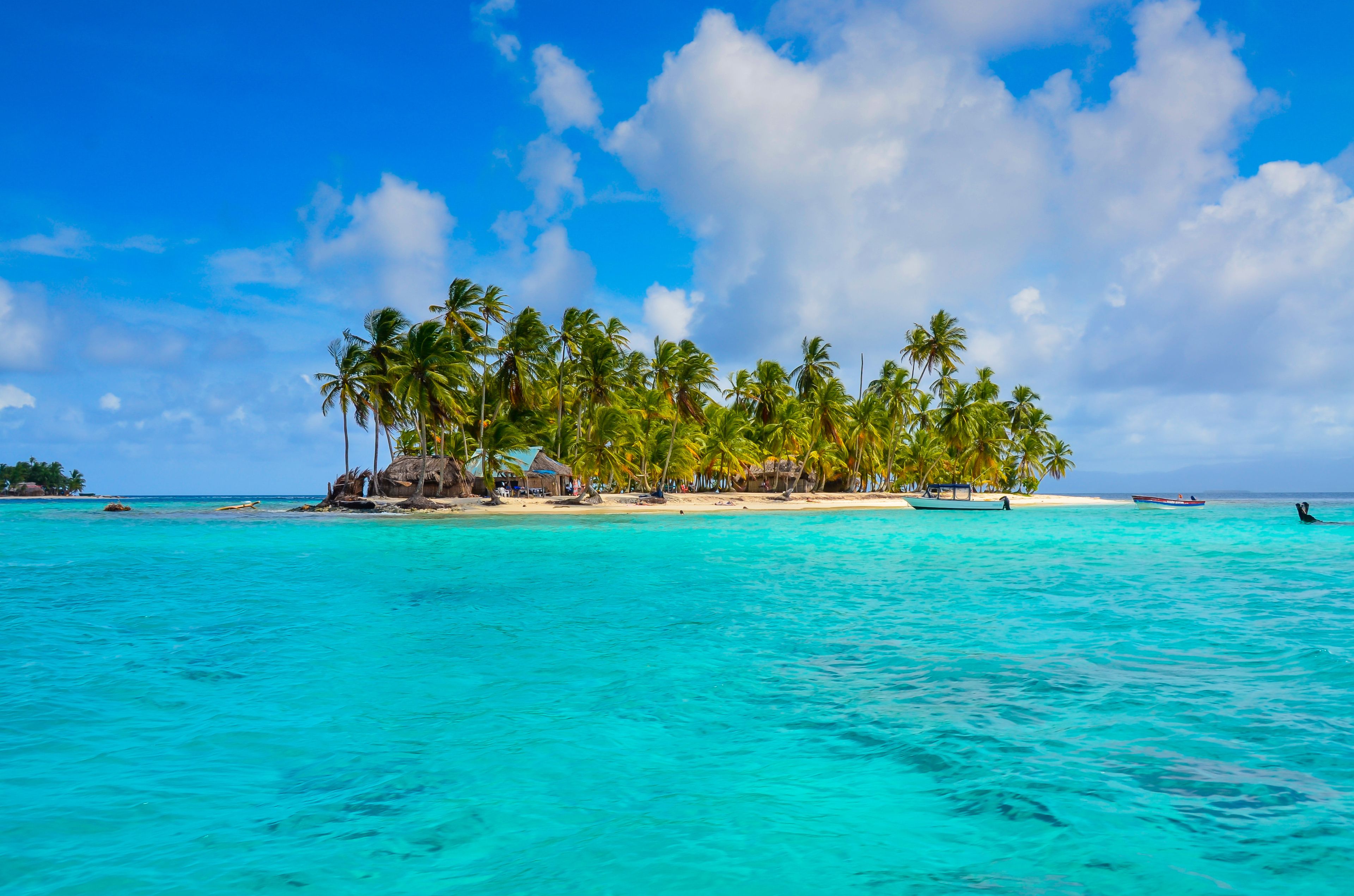 A tropical island with clear turquoise waters, palm trees, and thatched-roof huts.