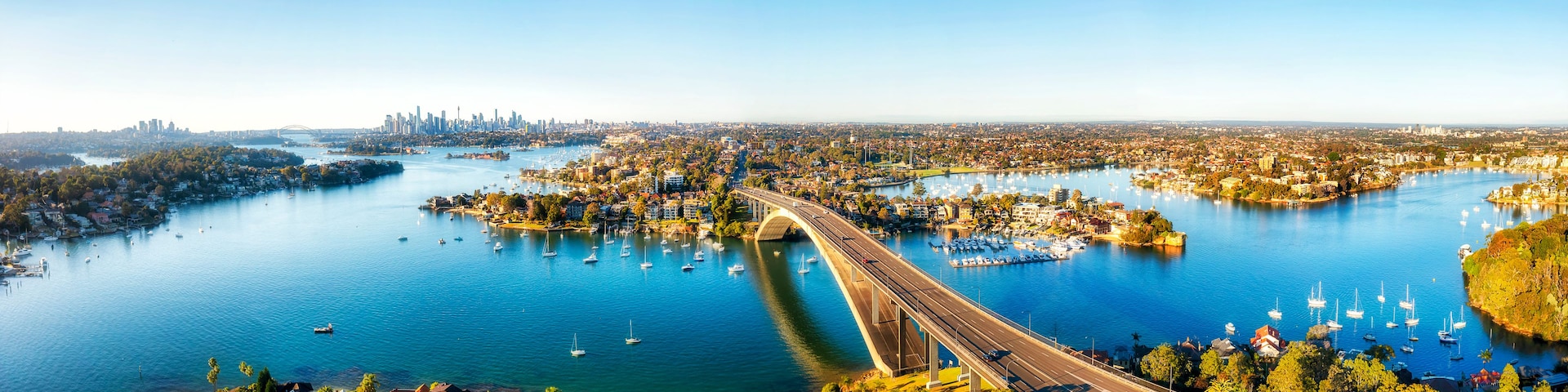 Eine Küstenstadtlandschaft mit einer markanten Brücke, einem Yachthafen und einer modernen Skyline.