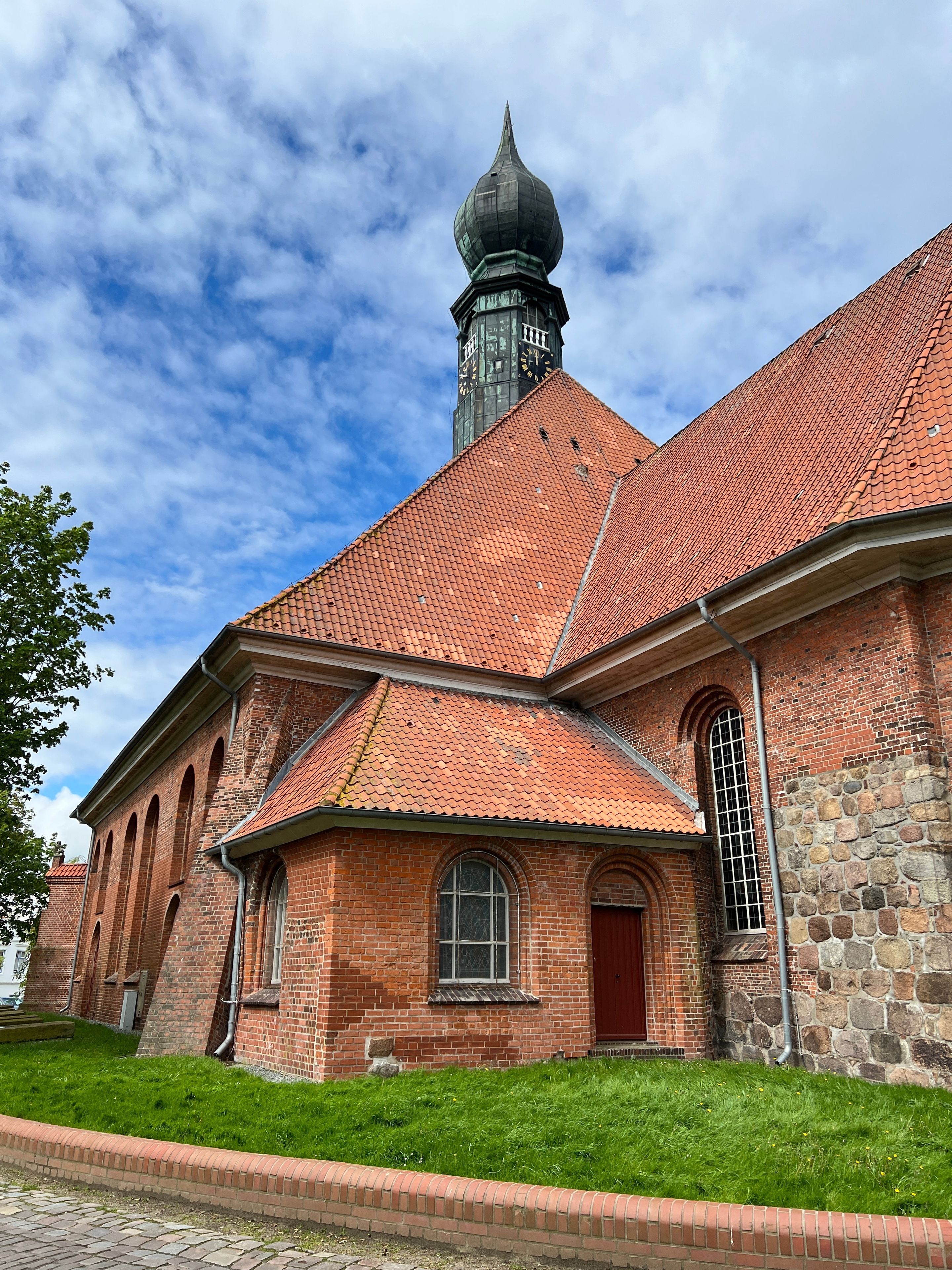 En murstenskirke med rødt tegltag, et klokketårn og en stenvæg.