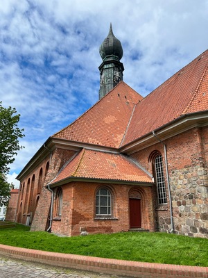 En murstenskirke med rødt tegltag, et klokketårn og en stenvæg.