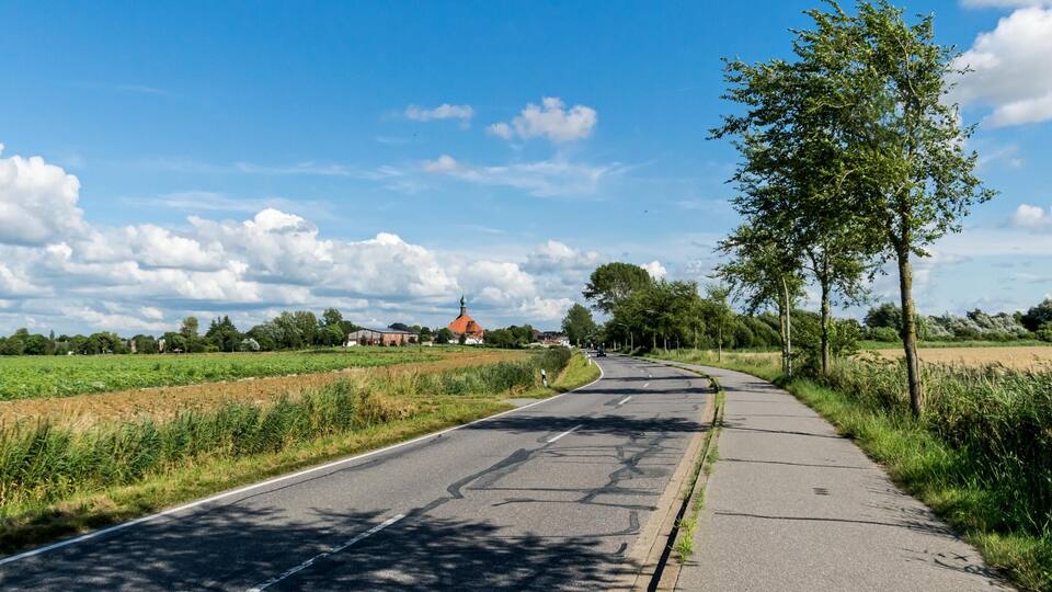 A rural road curving through fields with a church in the distance.