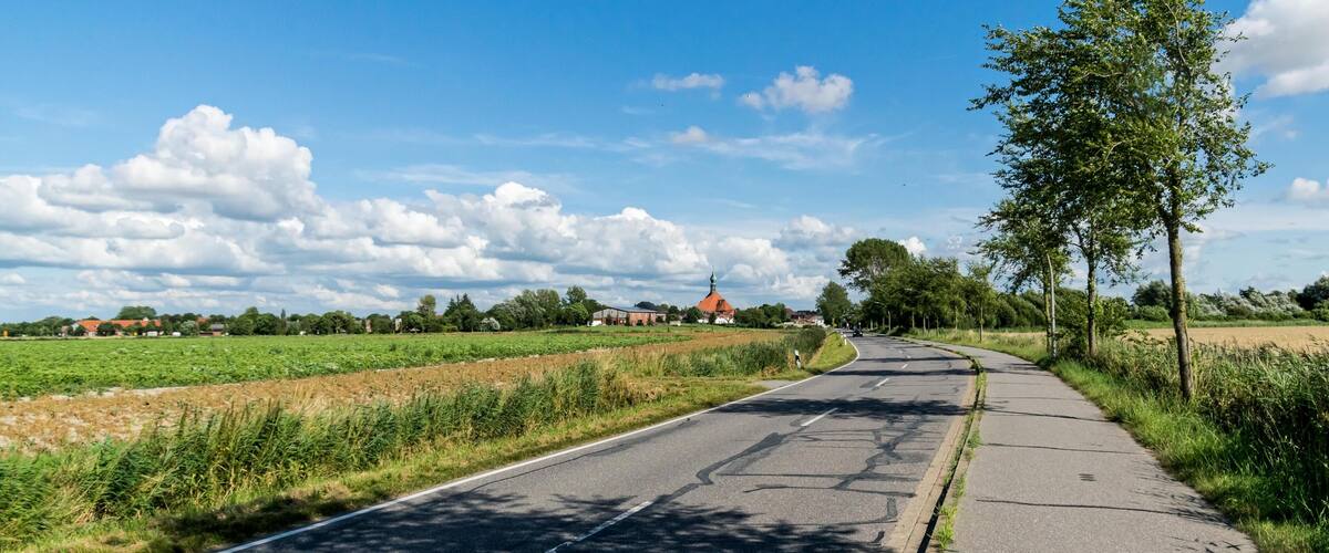 A rural road curving through fields with a church in the distance.