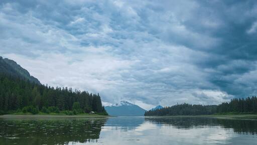 A house, forests, mountains, gray clouds can be seen from the boat on the river. Various landscapes in summer.Alaska, USA., 2017