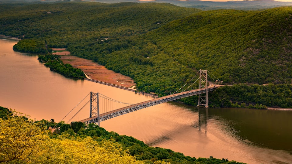 A suspension bridge over a river, surrounded by lush green hills.