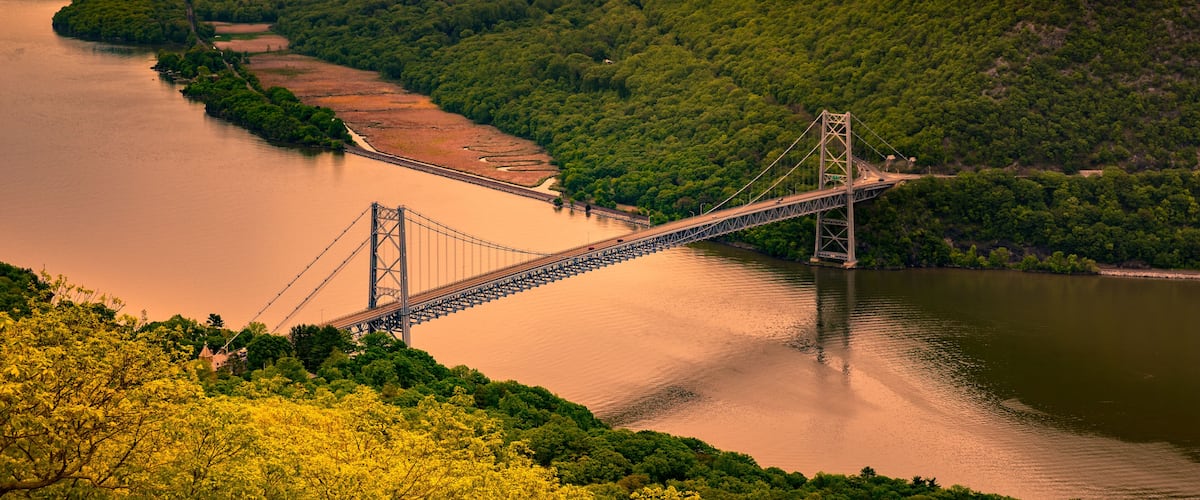A suspension bridge over a river, surrounded by lush green hills.