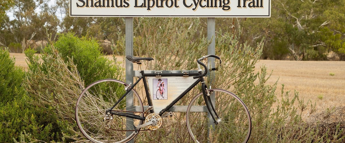 A sign for the Shamus Liptot Cycling Trail with a bicycle mounted on a stand.