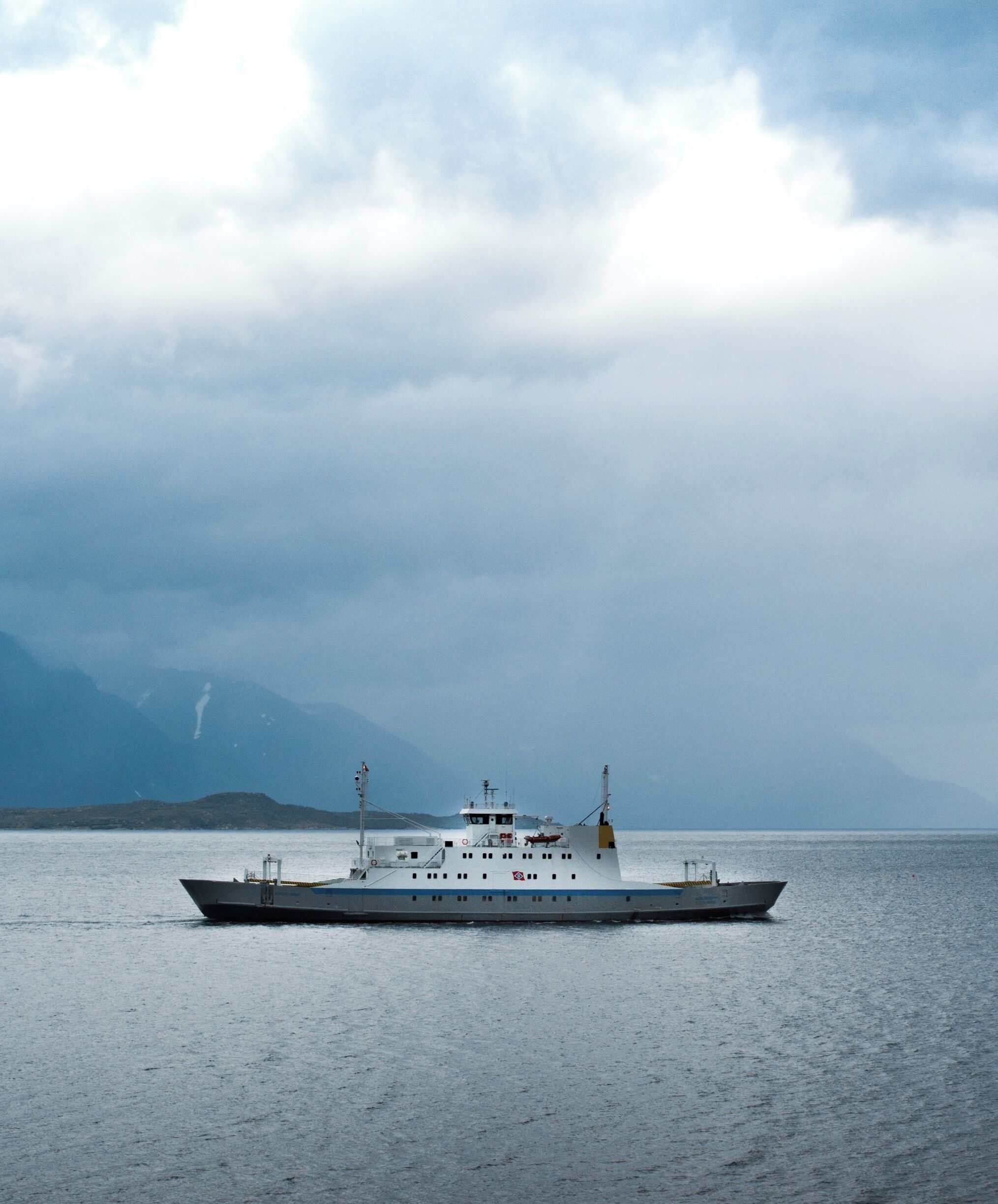 A large ship on calm waters with a mountainous backdrop.