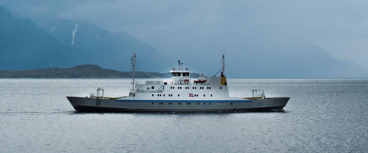 A large ship on calm waters with a mountainous backdrop.