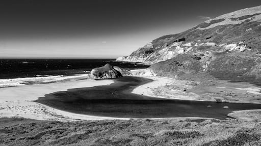 Dramatic image of the Little Sur River running and winding into the Pacific Ocean off of highway 1, California with white sandy beach and waves.